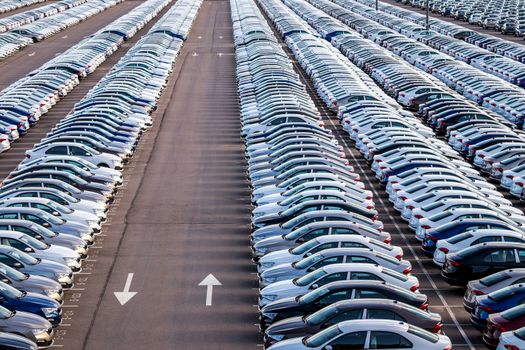 Rows of a new cars parked in a distribution center on a car factory on a sunny day. Parking in the open air.