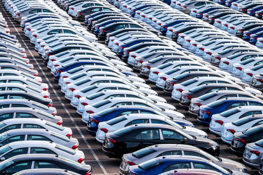 Rows of a new cars parked in a distribution center on a car factory on a sunny day. Top view to the parking in the open air.