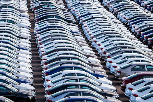 Rows of a new cars parked in a distribution center on a car factory on a sunny day. Top view to the parking in the open air.