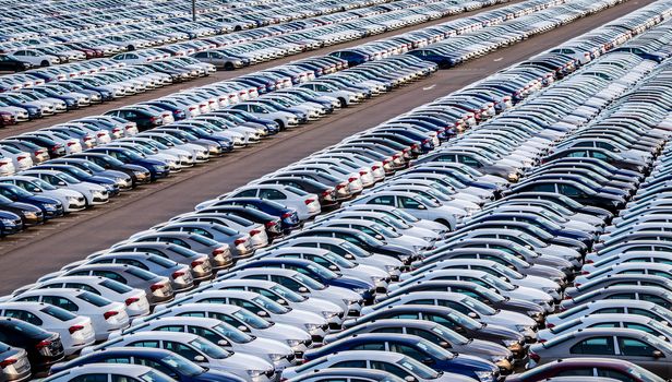 Rows of a new cars parked in a distribution center on a car factory on a sunny day. Top view to the parking in the open air.