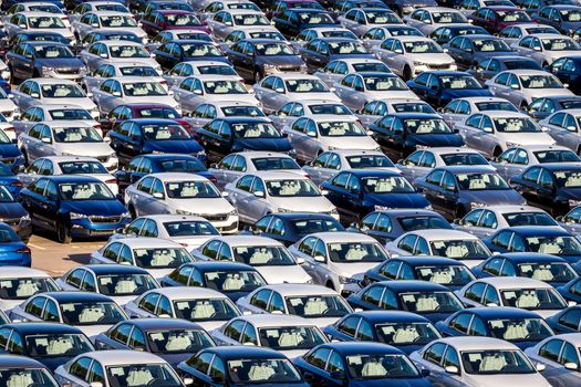 Rows of a new cars parked in a distribution center on a car factory on a sunny day. Top view to the parking in the open air.