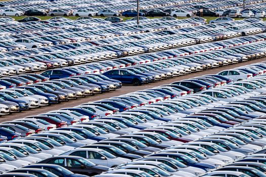 Rows of a new cars parked in a distribution center on a car factory on a sunny day. Parking in the open air.