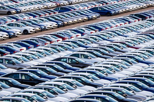 Rows of a new cars parked in a distribution center on a car factory on a sunny day. Top view to the parking in the open air.