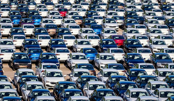 Rows of a new cars parked in a distribution center on a car factory on a sunny day. Parking in the open air.