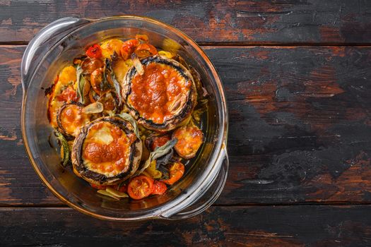 Portobello baked with cheddar cheese, cherry tomatoes and sage in glass pot on old wooden background top view space for recipe or text