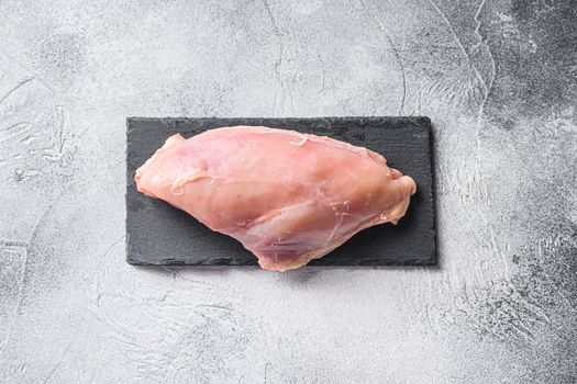 Raw chicken breast fillets on stone board over grey background.