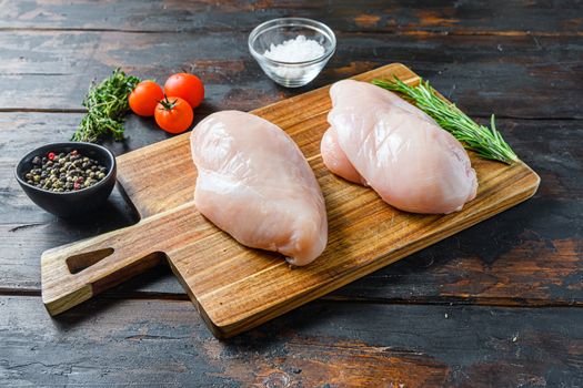 Raw chicken breasts and spices on wooden cutting board on old dark table side view