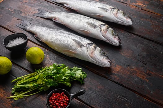 Fresh raw european bass with spices and herbs ingredients on old fisherman dark wooden table side view space for price.
