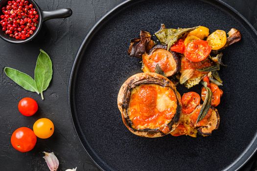 Served portobello mushrooms,baked and stuffed with ingredients cheddar cheese, cherry tomatoes and sage on black plate over black background top view. High quality.