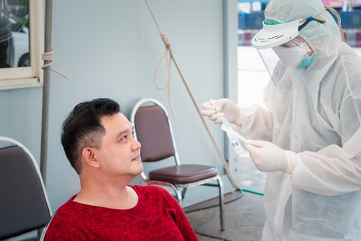 Doctor in PPE suit and asian man patient check by COVID-19 specimen performing a nasopharyngeal or oropharyngeal swab from nasal and oral at hospital