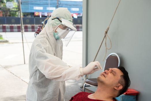 Doctor in PPE suit and asian man patient check by COVID-19 specimen performing a nasopharyngeal or oropharyngeal swab from nasal and oral at hospital