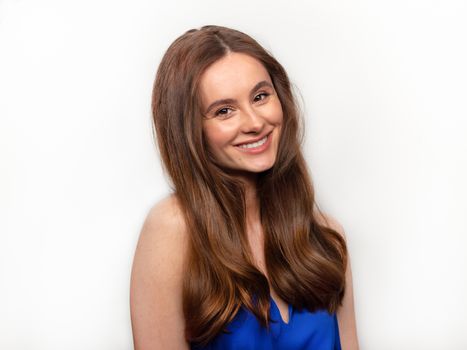 Close up shot of stylish young woman in blue dress smiling in front of white background. Beautiful female model with copy space.