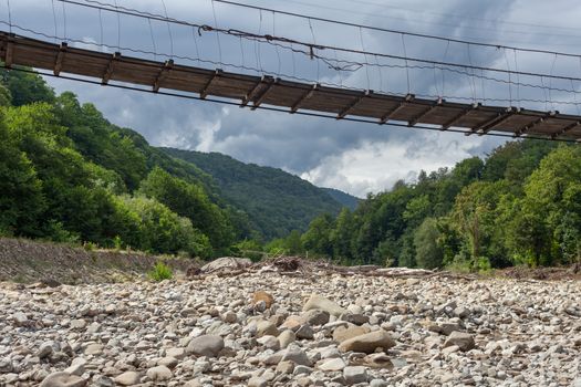 Suspension bridge over the mountain river at the summer cloudy day