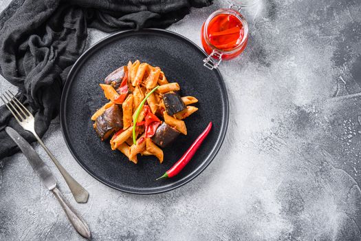 Aubergine penne eggplant pasta, pepper tomatoe sauce, on black plate overgrey concrete background served top view space for text