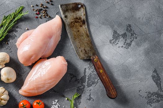 Raw organic chicken breast with meat butcher cleaver on a grey background. Food preparation, top view space for text