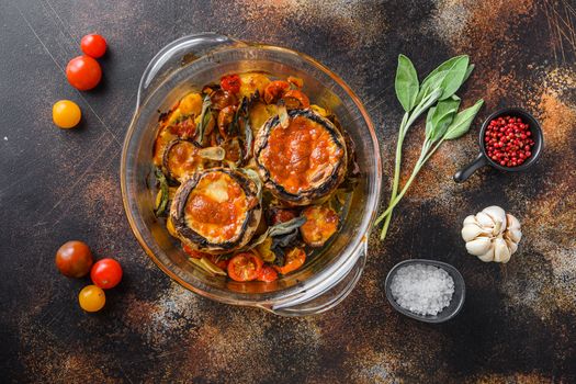 Portobello mushrooms,baked with cheddar cheese, cherry tomatoes and sage in glass pot on old rustic metall dark background top view