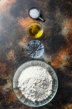 Ingredients for the dough, flour oil water and salt on darkbackground