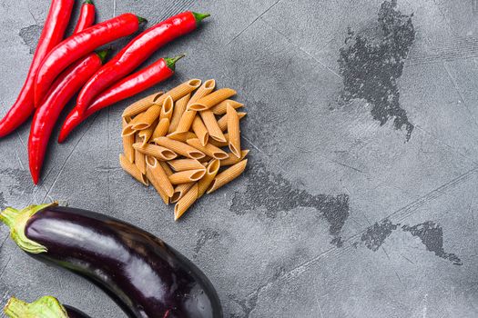 Penne pasta ingredients eggplant pasta, pepper tomatoe sauce, on grey background stop view space for text