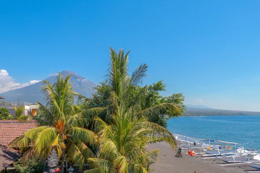 Sunset on the beach on a tropical island. Orange colored sky and clouds. Big majestic volcano on the horizon. Quiet sea and romantic atmosphere.