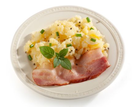 Mashed potatoes with fried bacon, basil and green onion on the white plate