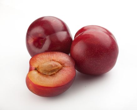 Two whole red plums and half plumы with bone on the white