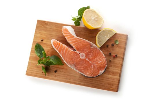 Raw steak of salmon with fresh lemon and basil on the wooden board