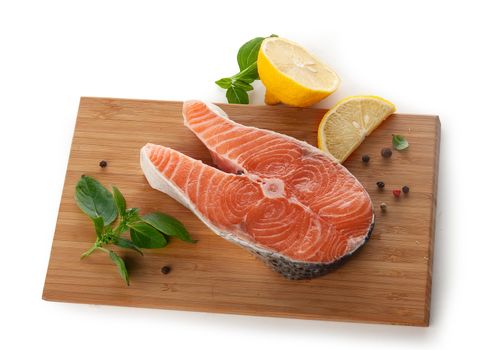 Stake of salmon with fresh basil and lemon on the wooden board