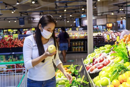 Asian woman wearing protective face mask push and hold shopping cart in supermarket department store. Girl, looking grocery to buy  some fruit. New normal after covid-19. Family concept.