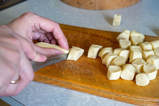 cook slices dough into pieces on a wooden board