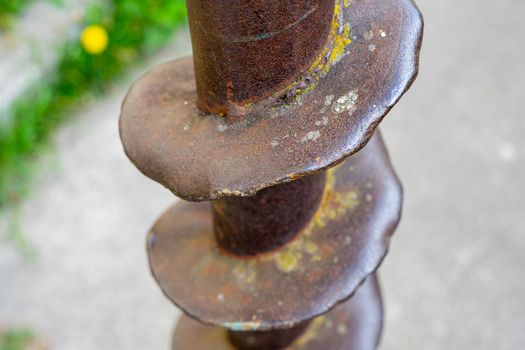 Part of an old rusty drill drilled into the ground . Metal rusty drill