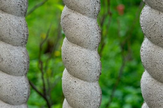 Part of a concrete fence in the form of a pigtail. Blurred green background