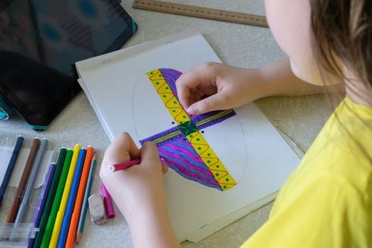 The girl draws a picture in the album with felt-tip pens. Felt-tip pens and tablet on the table near the child