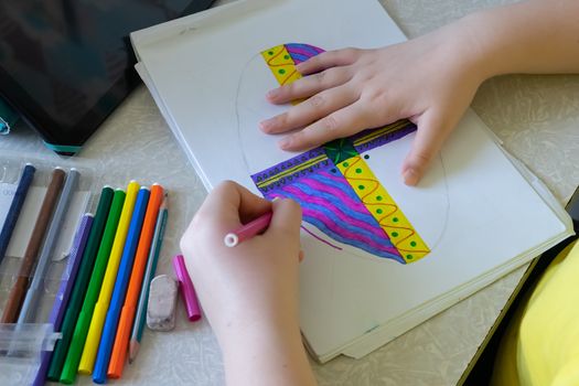 The girl draws a picture in the album with felt-tip pens. Felt-tip pens and tablet on the table near the child