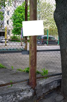 Basketball court fenced with a net. On the pillar hangs a sign for the inscription