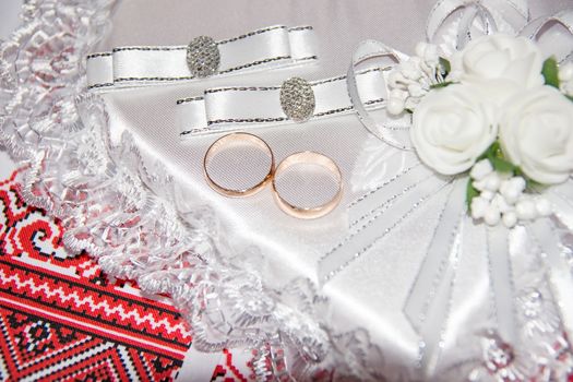 Wedding rings lie on a pillow in the form of a heart. Boutonniere and wedding rings. Ukrainian wedding embroidery close up.