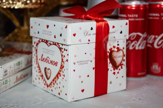 Ukraine, Vinnytsia - May 23, 2020 Gift box with candy tied with a red ribbon and Coca-Cola in the background