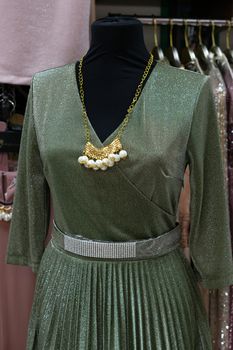 Green dress with a belt hanging on a mannequin. Retail trade