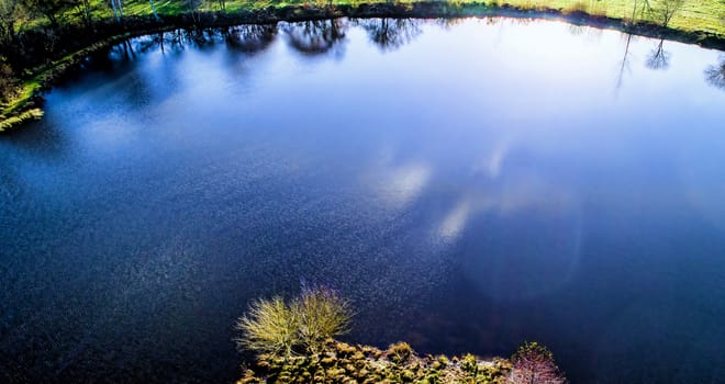 Pond in the back light with the reflections of the sun in the water, aerial photograph with the drone, intensified colours