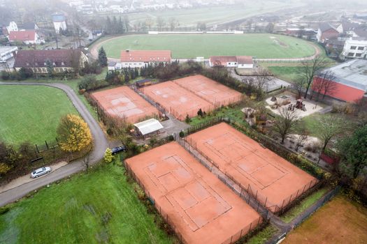 Aerial view of tennis courts during autumn with dismantled nets. Football field with lawn in the background, uptake with drone from 50 meters height
