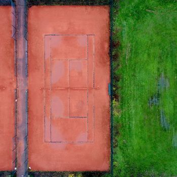 Tennis court with red gravel next to a lawn, abstract effect by vertical aerial photograph with drone