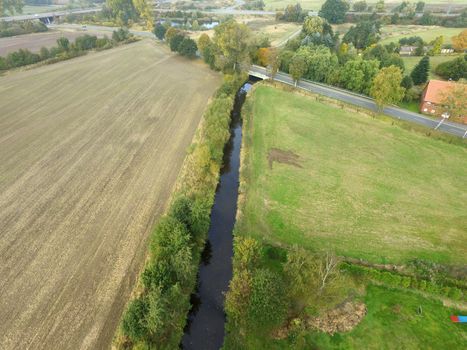 Aerial photograph of a straightened unnatural stream between fields and meadows, made by drone