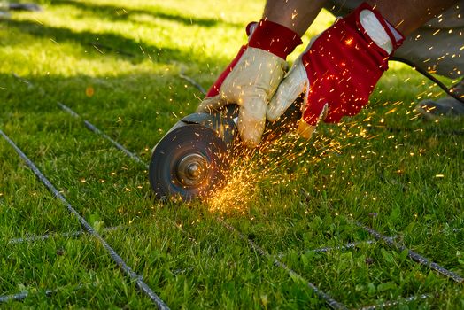 Cutting metal net with grinder on green grass. Sparks from contact materials. Worker outside, cut the steel net. Process with angle grinder