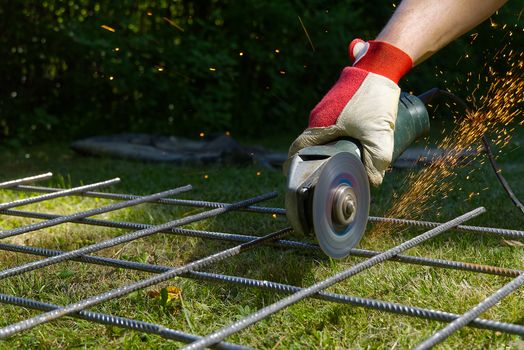 Cutting metal net with grinder on green grass. Sparks from contact materials. Worker outside, cut the steel net. Process with angle grinder