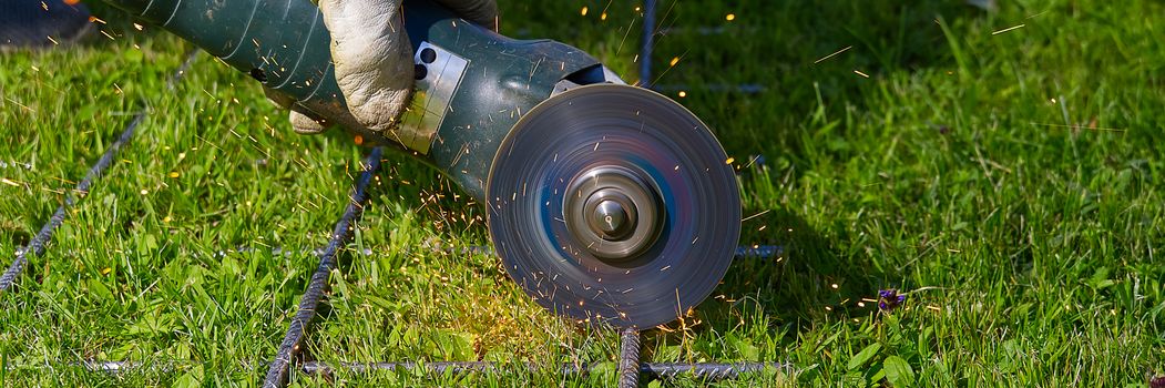 Cutting metal net with grinder on green grass. Sparks from contact materials. Worker outside, cut the steel net. Process with angle grinder