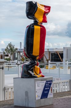 Knokke-Heist, Flanders, Belgium -  June 16, 2019: Knokke-Zoute part of town. Closeup of statue of candy wrapped in Belgian flag standing on pedestal adjacent to beach. Cloudscape.