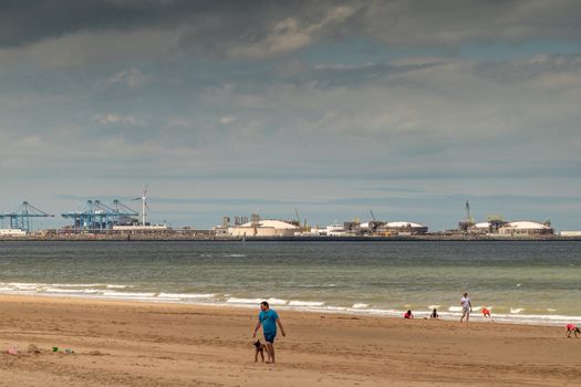 Knokke-Heist, Flanders, Belgium -  June 16, 2019: Knokke-Zoute part of town. View from sandy beach on LNG sea terminal and container cranes of Port of Zeebrugge. People on sand. Greenish Nord Sea,