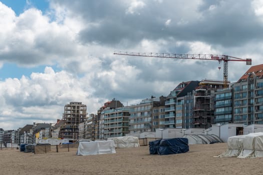 Knokke-Heist, Flanders, Belgium -  June 16, 2019: Knokke-Zoute part of town. View from sandy beach on row of highrise apartments well and not under construction. White cabins on sand. Heavy cloudscape.