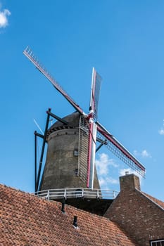 Sluis, the Netherlands -  June 16, 2019: The iconic brick-stone windmill, named Molen Van Sluis, and its four wings rises above red pane roofs and stands under full blue sky.