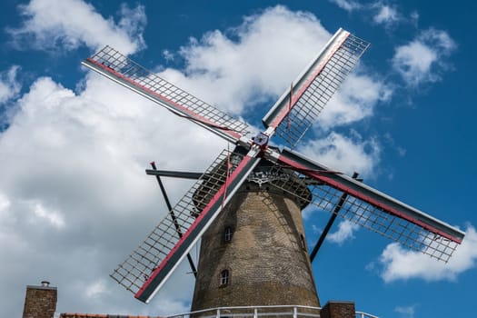 Sluis, the Netherlands -  June 16, 2019: The iconic brick-stone windmill, named Molen Van Sluis, and its four wings stands under deep blue sky with thick white clouds.
