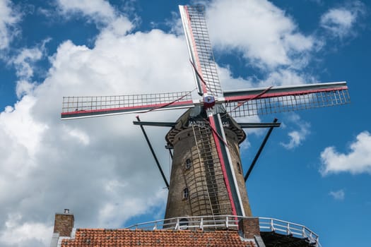 Sluis, the Netherlands -  June 16, 2019: The iconic brick-stone windmill, named Molen Van Sluis, and its four wings stands under deep blue sky with thick white clouds. Red roof at bottom.